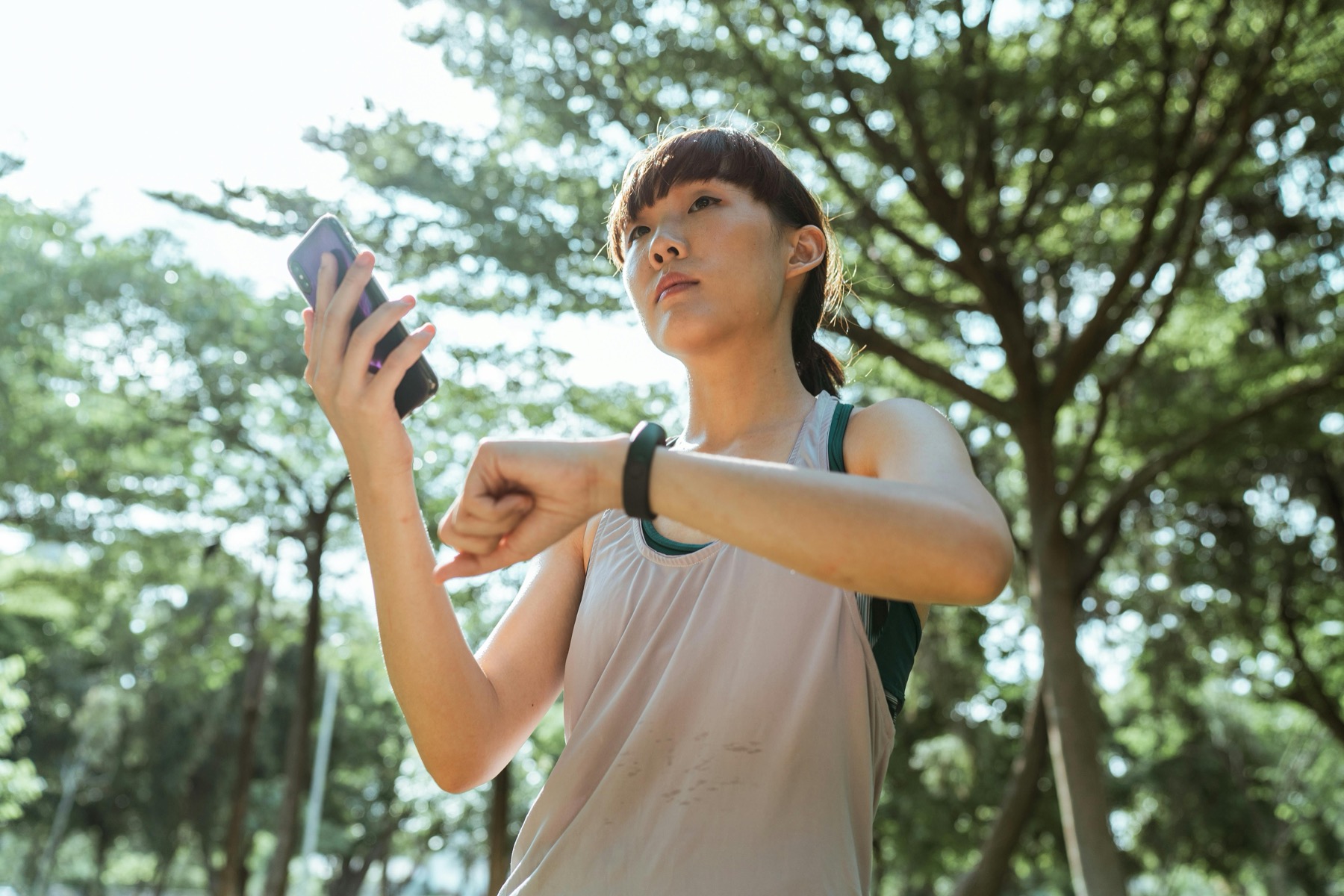 A woman wearing a smartwatch and checking her phone outdoors.