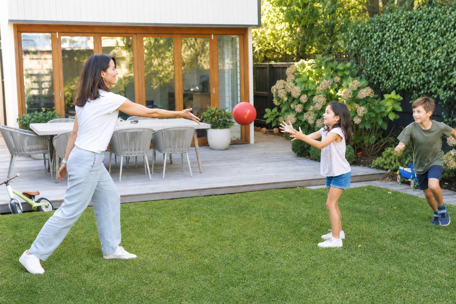 A mother plays ball with her children in their backyard.