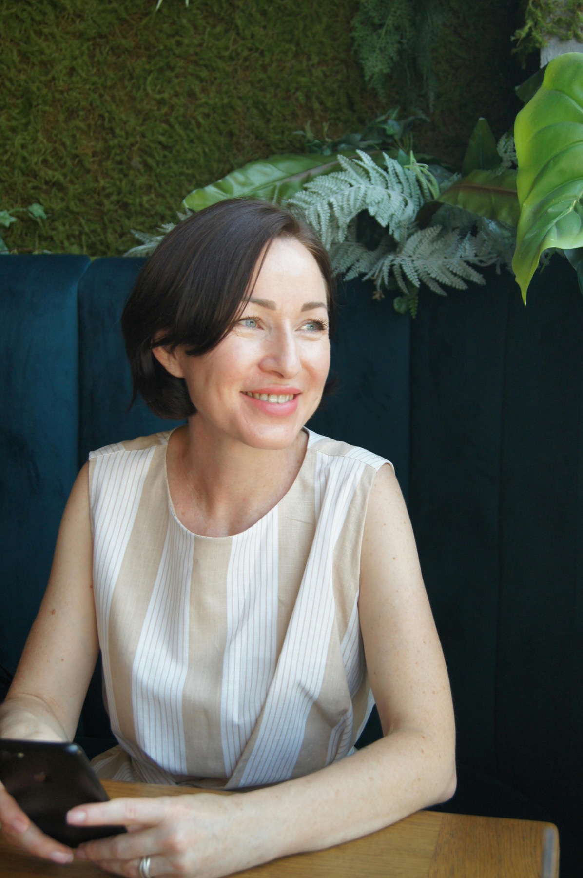 A woman sitting in a quiet cafe, holding her phone with a calm expression.